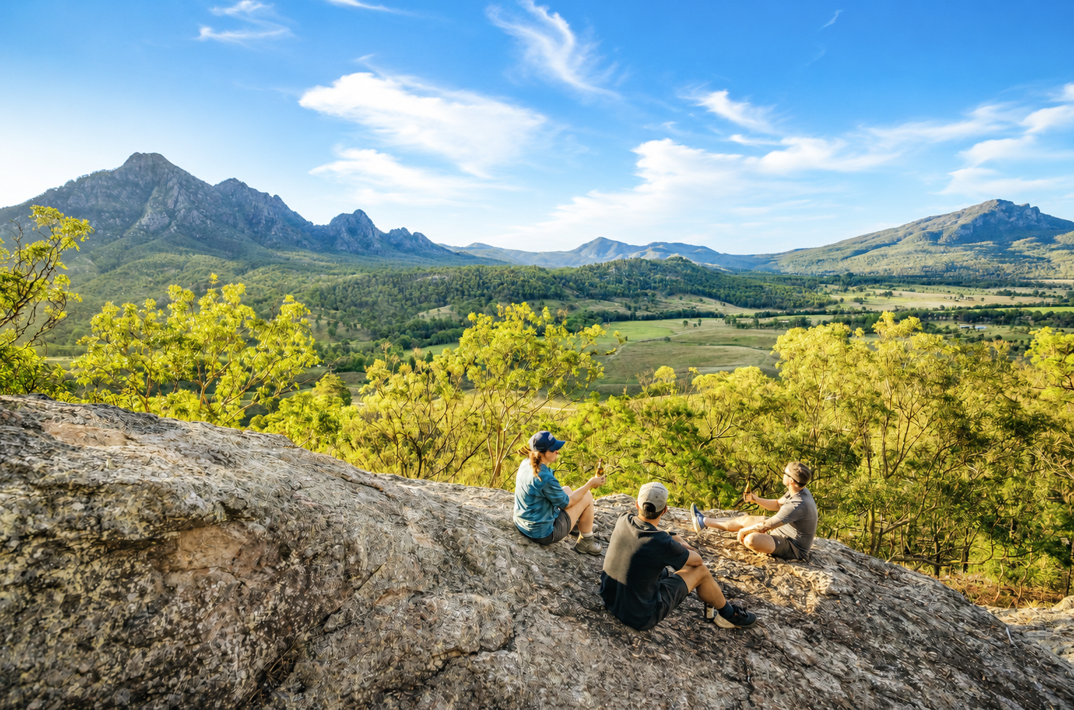 People resting on a rocky outcrop overlooking a lush green valley and mountains